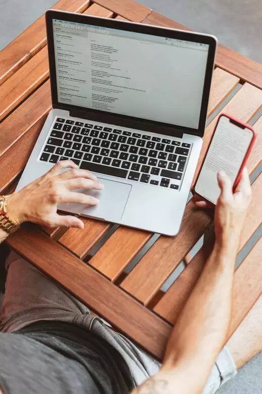 A stock image showing a man at a table on his laptop and smart phone